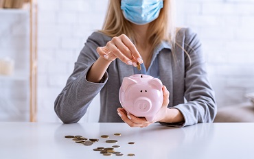 Business woman with mask puts money into piggy bank