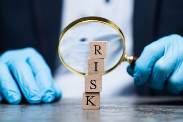 Hands with gloves and a magnifier looking at a pile of cubes with letters RISK