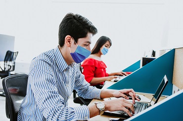 A young male and female with masks working with computers