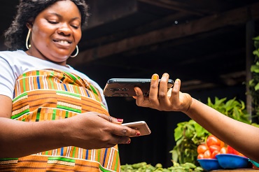 African lady selling in a local market receiving payment via contactless transfer of funds from a customer using their mobile phones