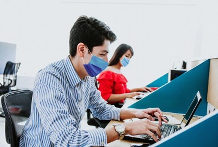 A young male and female with masks working with computers