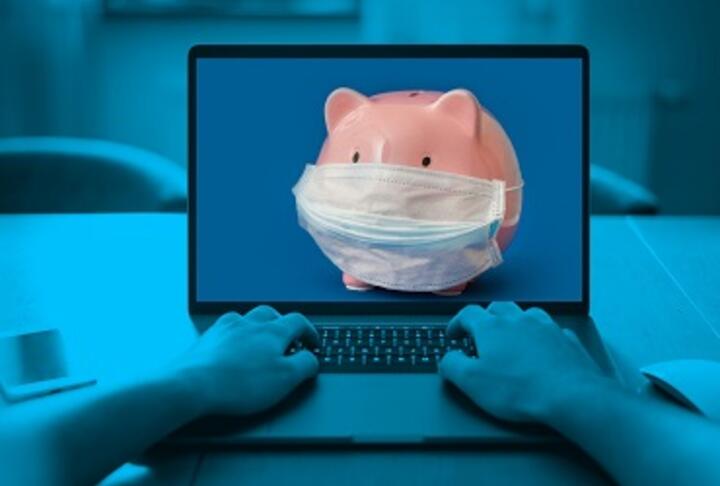 Two hands typing on a laptop and a piggy bank with mask on laptop screen