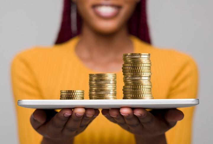 African lady with yellow shirt holding a tablet with coin stack on top